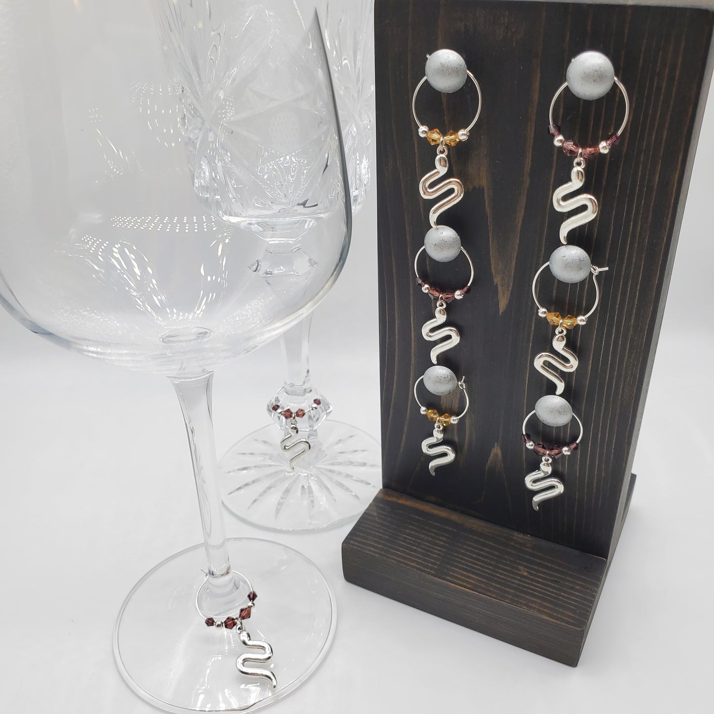 snake wine charms with crystal beads on a wooden charm holder and two glasses on the left with the same wine charms on each