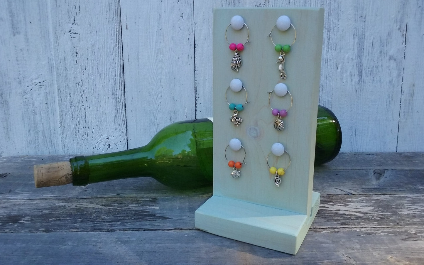 washed turquoise wine charms wooden stand with nautical wine charms and green bottle behind the stand